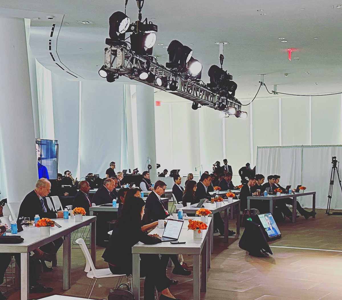 A group of professional investors and executives gathered for a meeting in the modern, sunlit lobby of a corporate headquarters.